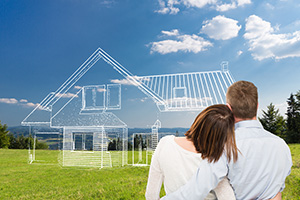 Couple with arms around each other look out over a field where a line drawn house is as designed with help by an Ocean County custom home builder.