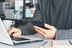 Person browsing a cell phone and a laptop highlighting the importance of adaptable Manahawkin web design
